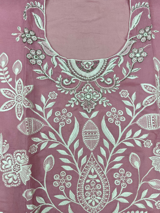 Close-up of a pink fabric with intricate white floral and paisley patterns.