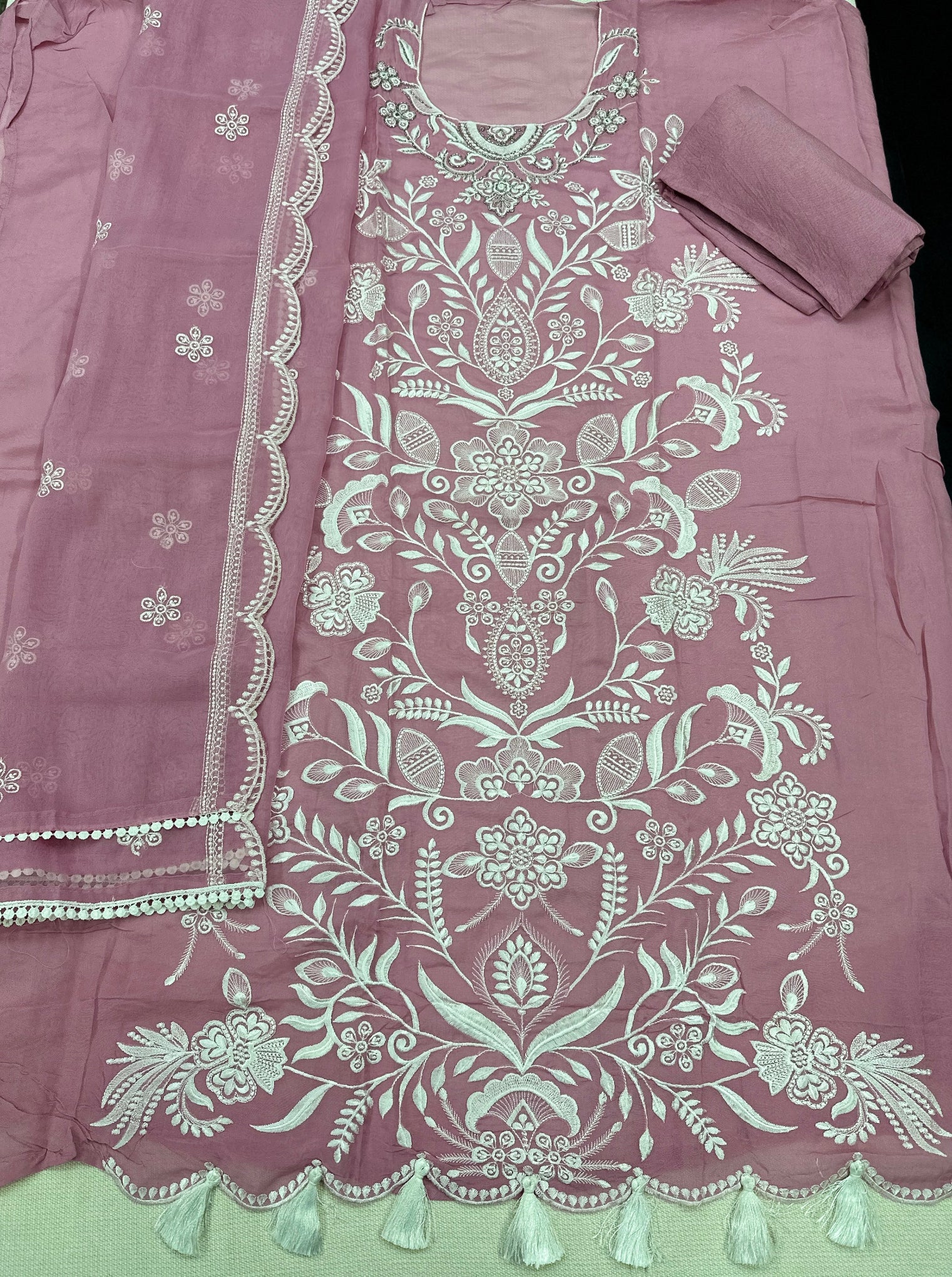 Pink fabric with intricate white embroidery and tassels 